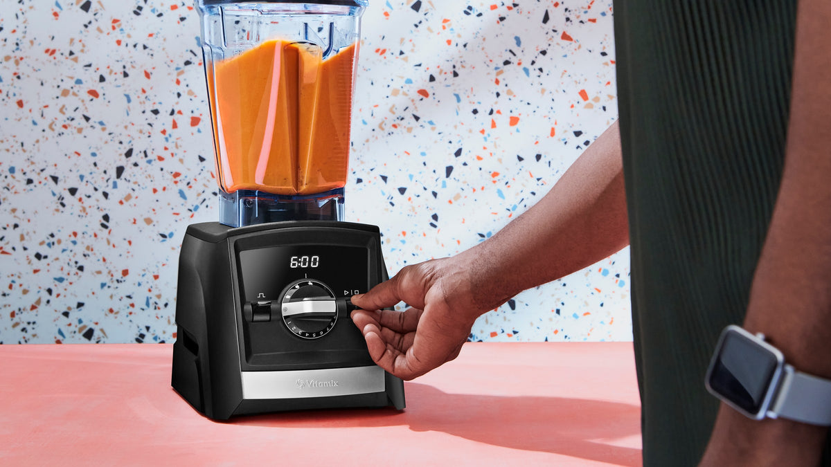 Vitamix Ascent A2500i auf der Kuechenzeile, Hand am Drehregler, Behaelter mit Karotten