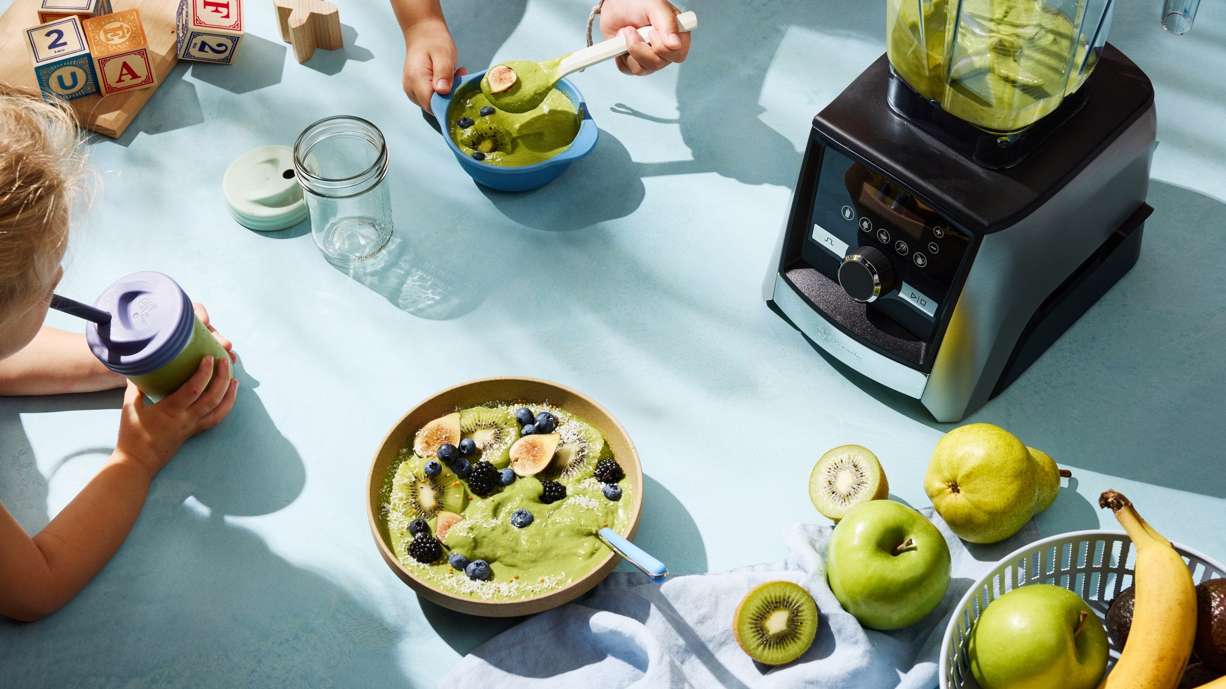 Vitamix Ascent A3500i am Familientisch neben einer gruenen Smoothie Bowl mit Obst