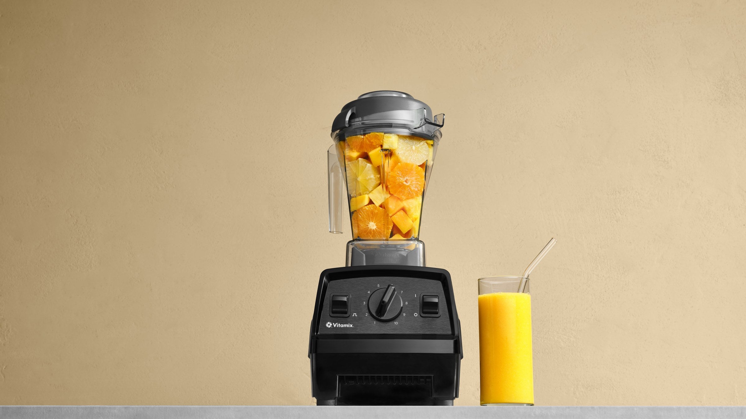 Vitamix Explorian mit dem 1,4-Liter-Classic-Behaelter voller Orangen, daneben ein Glas Saft