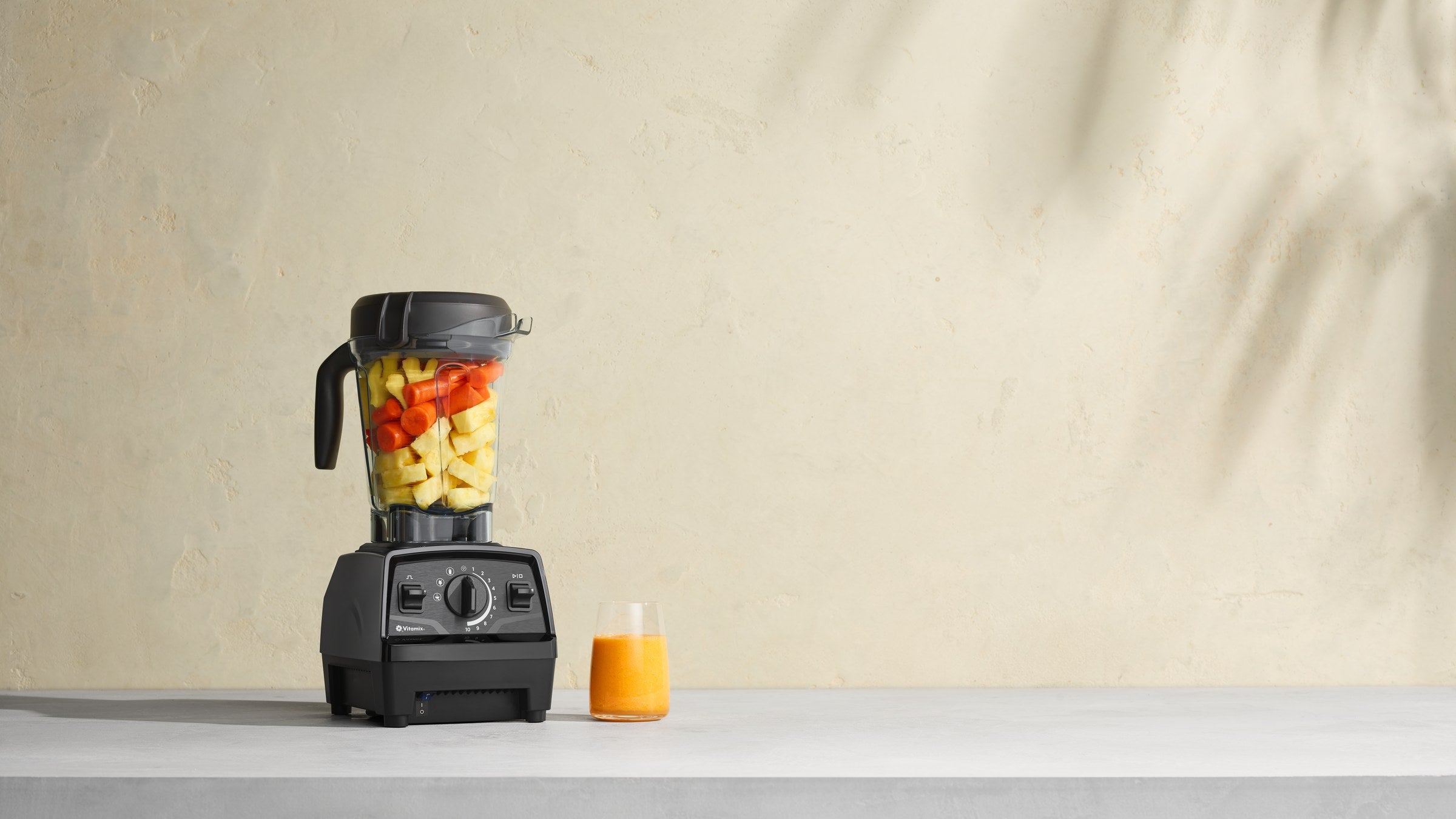Vitamix Explorian E520 mit Obst im Behaelter, daneben ein Glas Saft