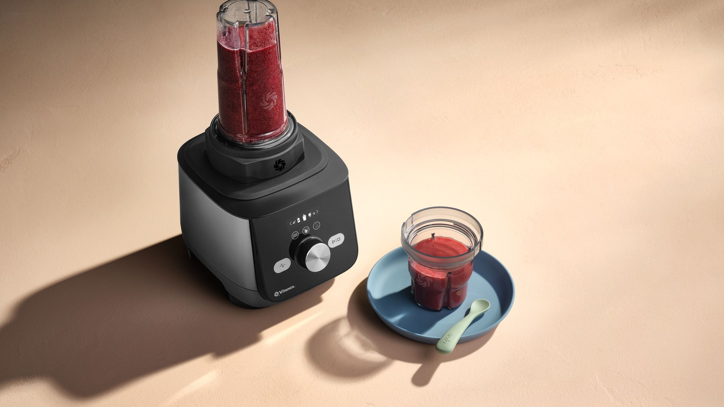 Vitamix To-Go Cup 600 ml auf dem Mixer, daneben ein Glas Beerensmoothie